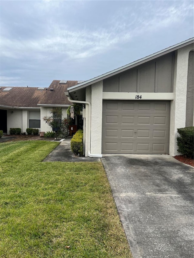 exterior space with a garage, stucco siding, concrete driveway, and a front yard