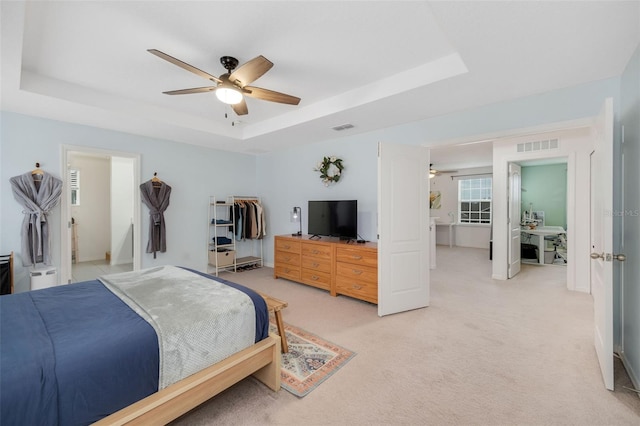 bedroom featuring a tray ceiling, light carpet, and ceiling fan