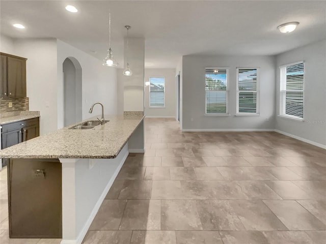 kitchen featuring sink, hanging light fixtures, a kitchen breakfast bar, light stone counters, and an island with sink