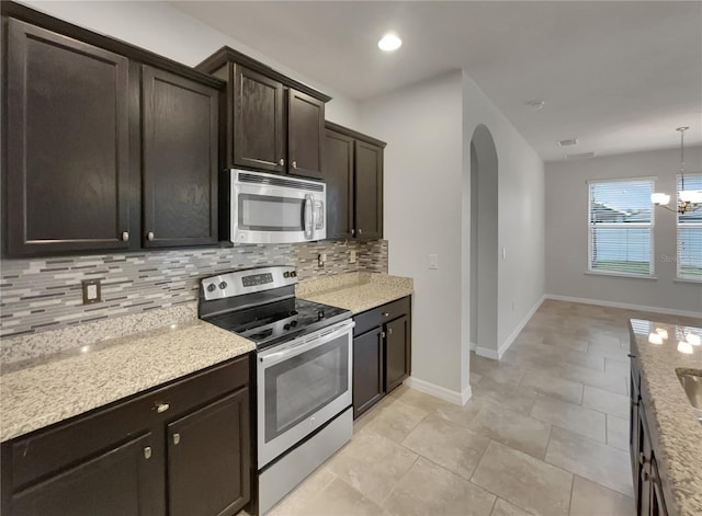 kitchen featuring an inviting chandelier, decorative backsplash, decorative light fixtures, light stone counters, and stainless steel appliances