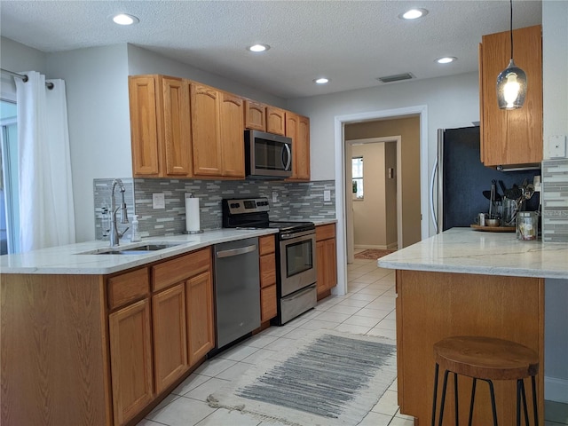 kitchen with sink, appliances with stainless steel finishes, tasteful backsplash, decorative light fixtures, and light tile patterned flooring