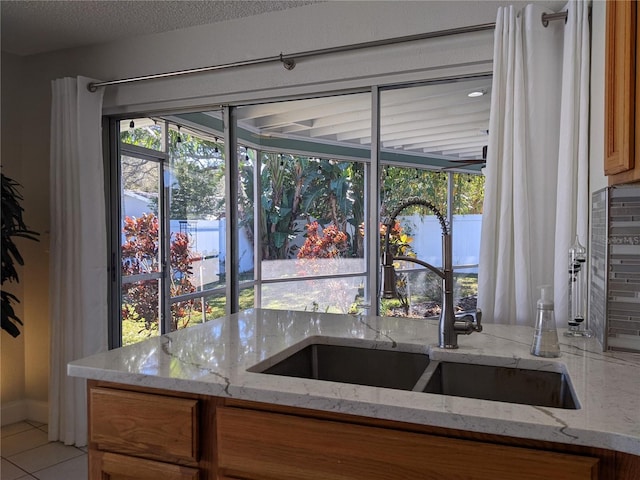 kitchen with a textured ceiling, light stone counters, light tile patterned floors, and sink