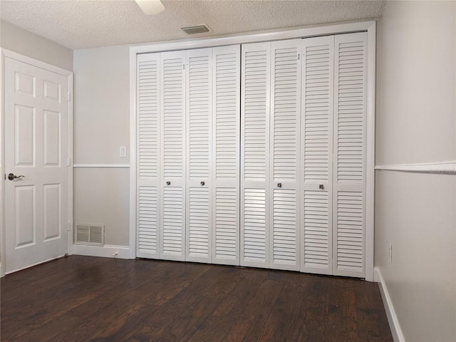 unfurnished bedroom with ceiling fan, a textured ceiling, and dark wood-type flooring