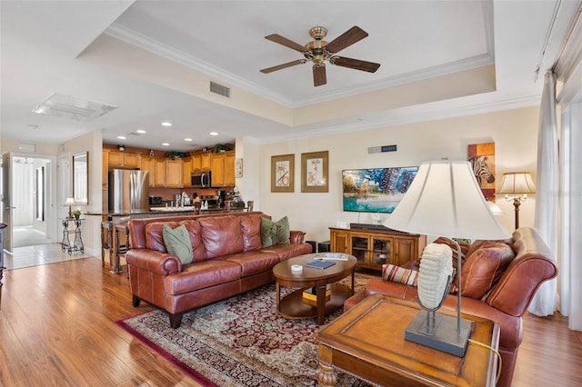 living room with crown molding, light hardwood / wood-style flooring, a raised ceiling, and ceiling fan