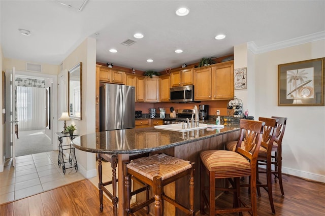 kitchen featuring sink, a breakfast bar area, dark stone countertops, stainless steel appliances, and light hardwood / wood-style floors