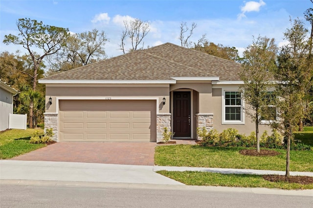 ranch-style house with stone siding, stucco siding, roof with shingles, decorative driveway, and a front yard