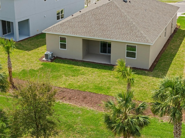 back of house with roof with shingles, central AC unit, a lawn, and stucco siding