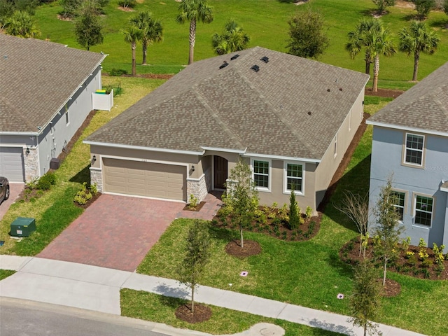 view of front of home with decorative driveway, stucco siding, a shingled roof, an attached garage, and stone siding