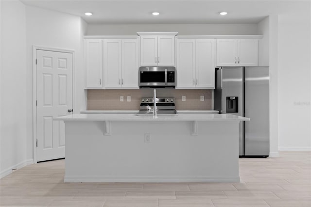 kitchen featuring an island with sink, tasteful backsplash, stainless steel appliances, and light countertops