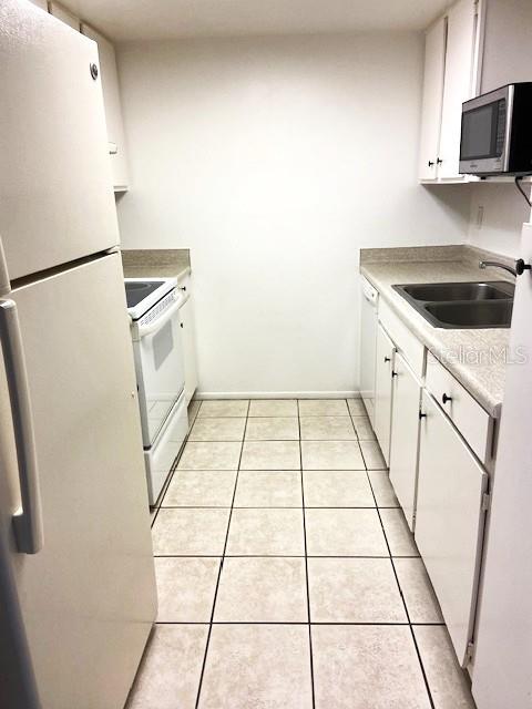 kitchen featuring white appliances, sink, light tile patterned floors, and white cabinetry