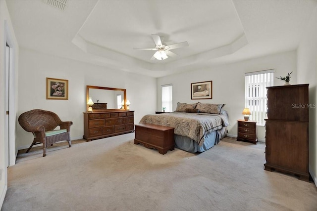 carpeted bedroom with ceiling fan and a raised ceiling