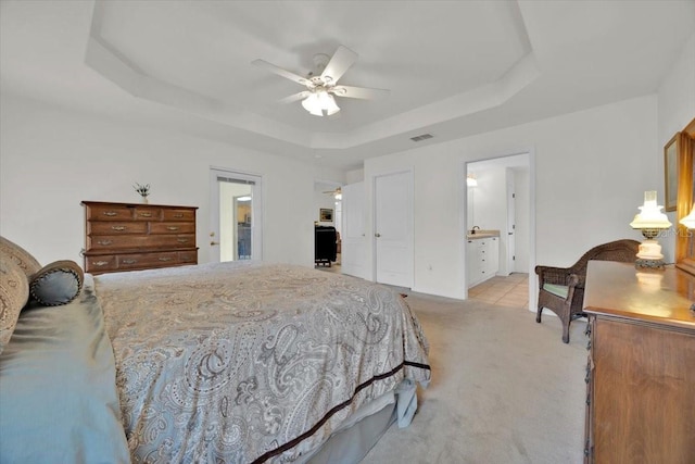 carpeted bedroom featuring ensuite bath, ceiling fan, and a tray ceiling