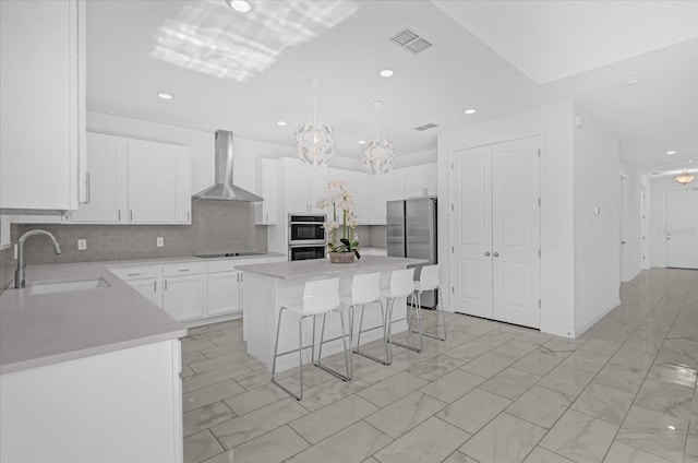 kitchen with a center island, sink, wall chimney range hood, white cabinets, and appliances with stainless steel finishes