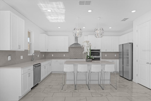 kitchen featuring wall chimney exhaust hood, white cabinetry, a kitchen island, and appliances with stainless steel finishes