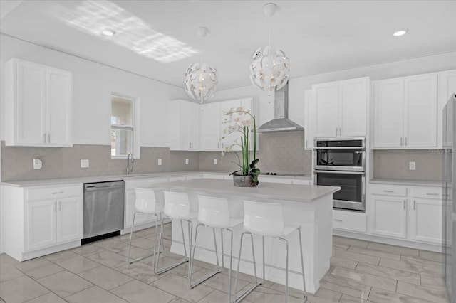 kitchen with wall chimney exhaust hood, white cabinetry, stainless steel appliances, and decorative light fixtures