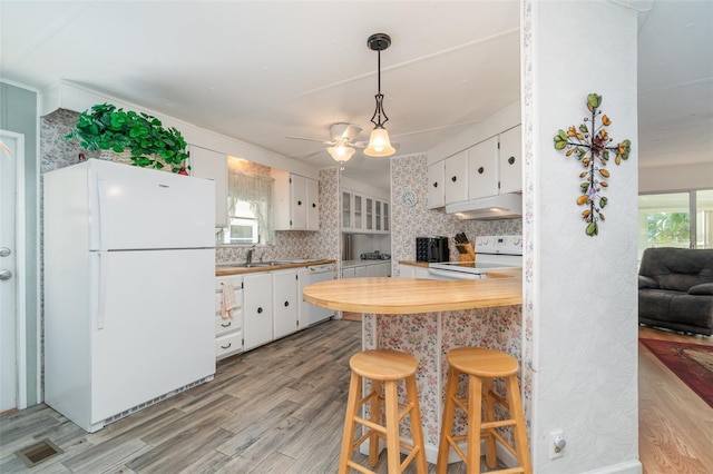 kitchen with white appliances, white cabinets, decorative light fixtures, tasteful backsplash, and light hardwood / wood-style floors