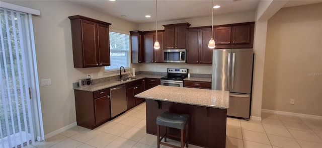 kitchen with light stone countertops, stainless steel appliances, sink, decorative light fixtures, and a kitchen island