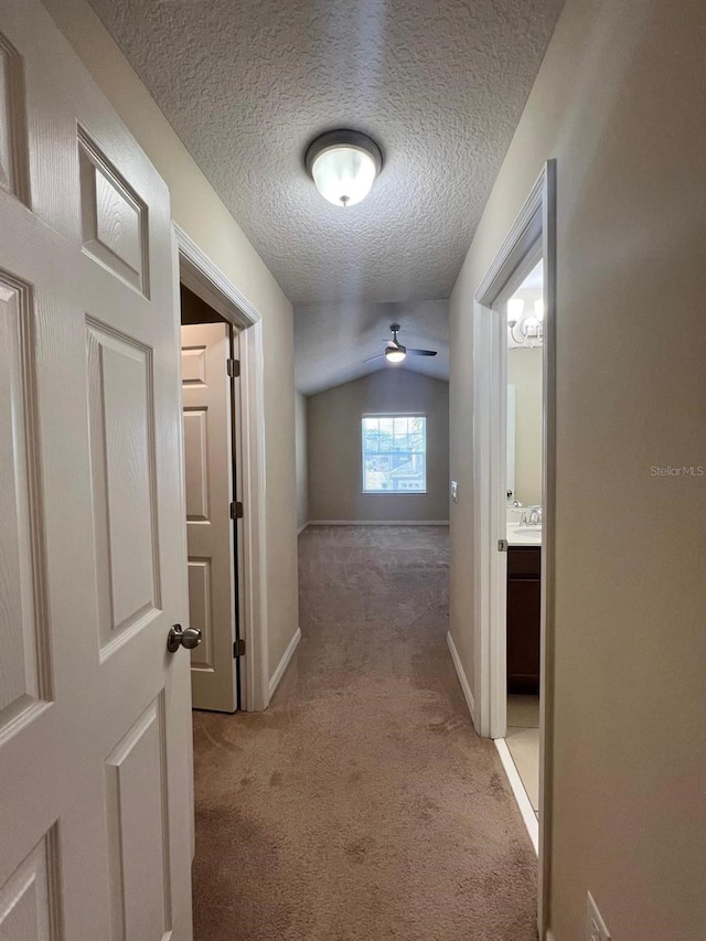 hallway with vaulted ceiling, light carpet, and a textured ceiling