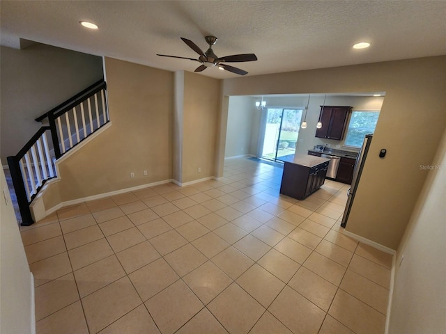 kitchen featuring ceiling fan, dark brown cabinets, a kitchen island, a textured ceiling, and light tile patterned flooring