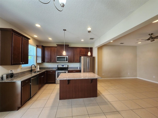 kitchen featuring sink, a breakfast bar, appliances with stainless steel finishes, a kitchen island, and decorative light fixtures