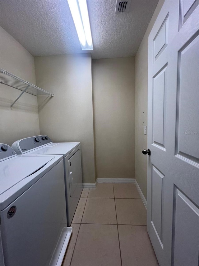 laundry area with washing machine and dryer, a textured ceiling, and light tile patterned flooring