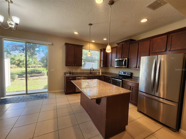 kitchen with light stone counters, appliances with stainless steel finishes, decorative light fixtures, and a kitchen island