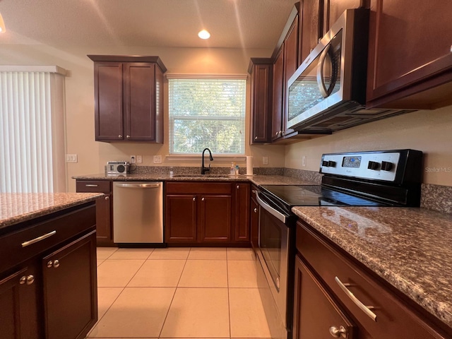 kitchen featuring light tile patterned flooring, sink, dark stone counters, dark brown cabinetry, and stainless steel appliances