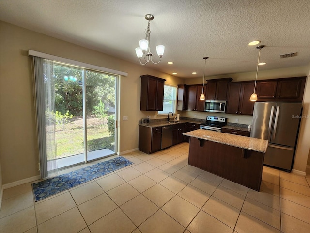 kitchen with sink, light stone counters, a center island, pendant lighting, and stainless steel appliances