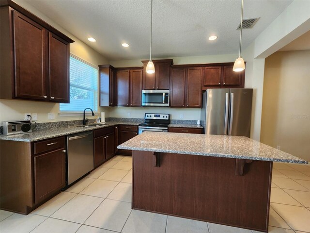 kitchen with a kitchen island, decorative light fixtures, sink, a kitchen bar, and stainless steel appliances