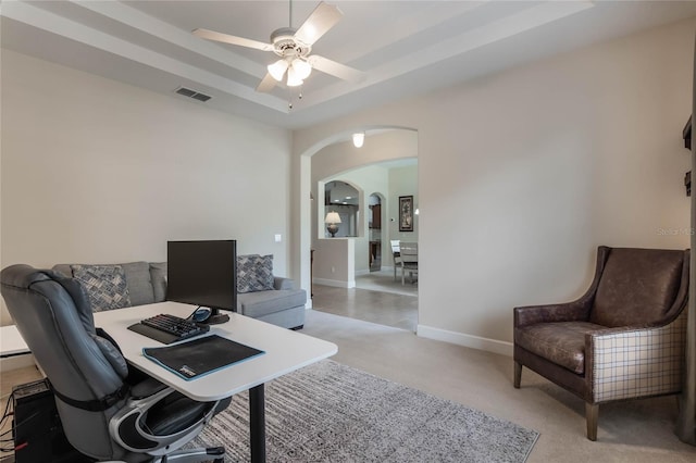 office featuring light colored carpet, ceiling fan, and a tray ceiling