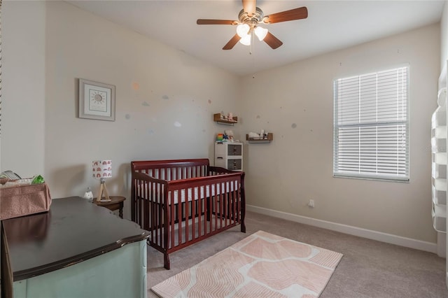 carpeted bedroom featuring ceiling fan and a crib