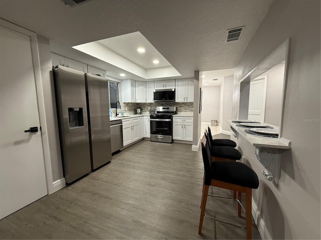 kitchen featuring sink, light hardwood / wood-style flooring, appliances with stainless steel finishes, a tray ceiling, and white cabinets