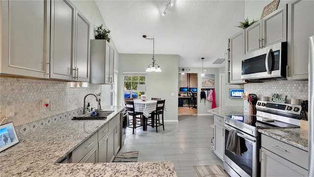 kitchen featuring gray cabinetry, sink, light stone counters, pendant lighting, and appliances with stainless steel finishes