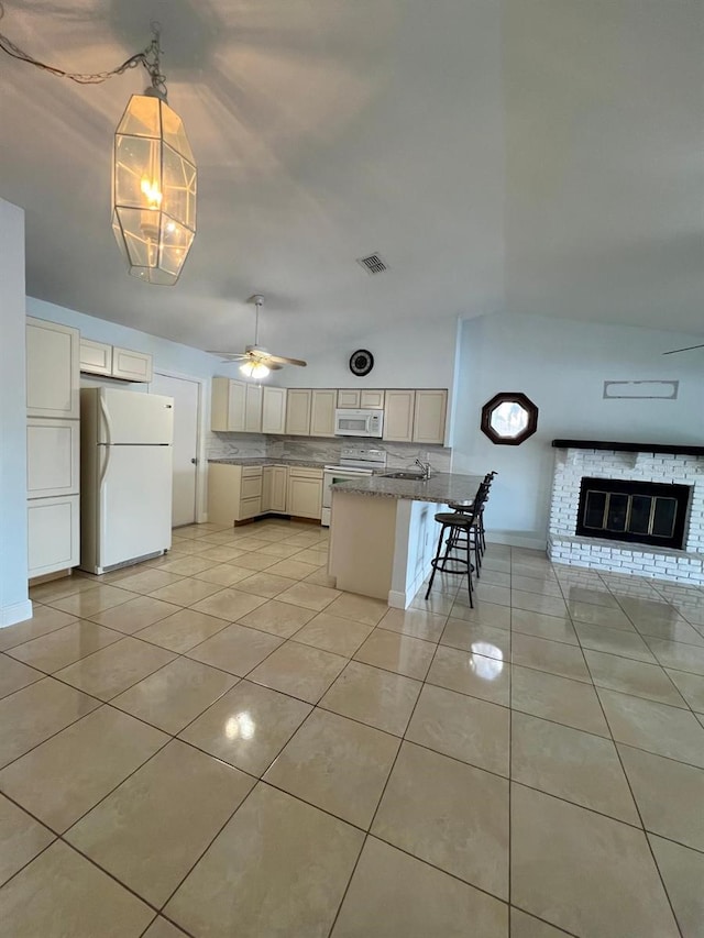 kitchen with ceiling fan, a brick fireplace, white appliances, a breakfast bar area, and a center island with sink