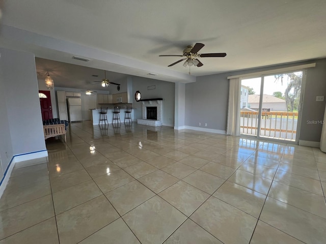 unfurnished living room with ceiling fan, light tile patterned flooring, and a brick fireplace