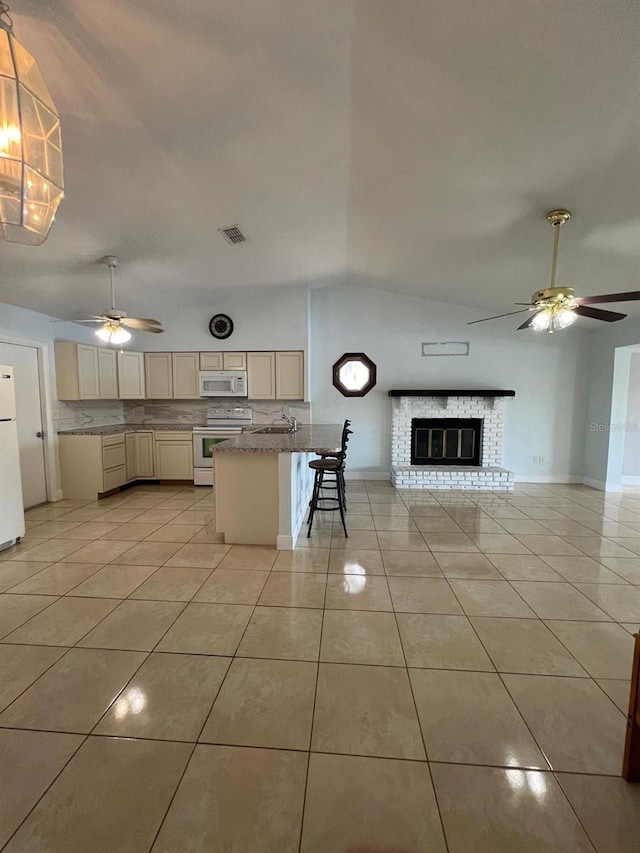 kitchen featuring tasteful backsplash, lofted ceiling, white appliances, a kitchen bar, and light tile patterned floors