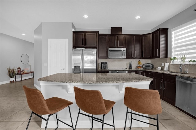 kitchen with light stone countertops, appliances with stainless steel finishes, a center island, and backsplash