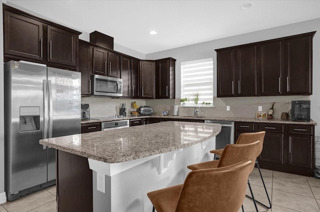 kitchen featuring a kitchen bar, light stone countertops, stainless steel appliances, a center island, and light tile patterned flooring