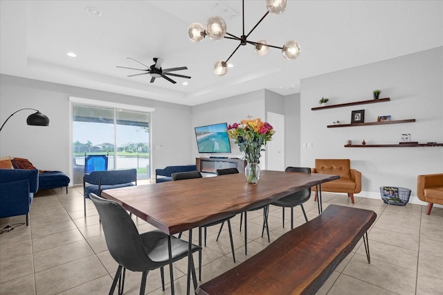 dining area featuring ceiling fan with notable chandelier, light tile patterned flooring, and a raised ceiling