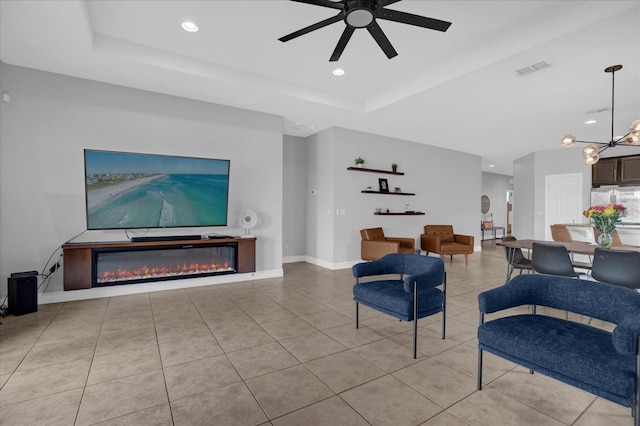 living room featuring ceiling fan with notable chandelier, light tile patterned floors, and a tray ceiling