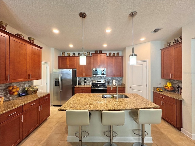 kitchen featuring sink, hanging light fixtures, appliances with stainless steel finishes, and an island with sink