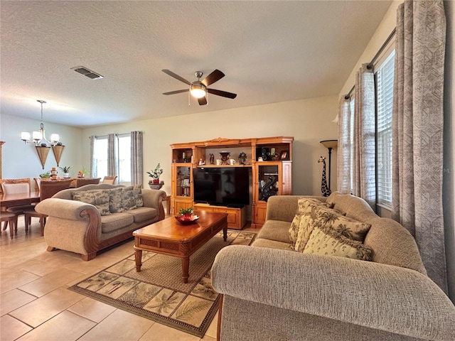 living room with a textured ceiling, light tile patterned floors, and ceiling fan with notable chandelier