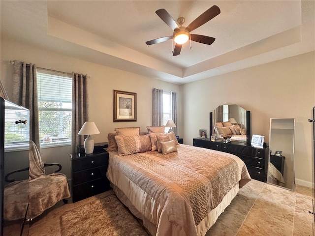 bedroom with a raised ceiling, ceiling fan, and multiple windows