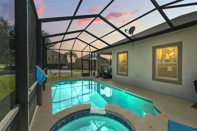 pool at dusk with glass enclosure, an in ground hot tub, and a patio area