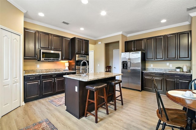 kitchen featuring a kitchen breakfast bar, a kitchen island with sink, appliances with stainless steel finishes, light wood-type flooring, and light stone counters