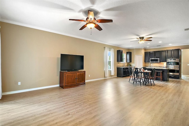 living room with ornamental molding, ceiling fan, and light wood-type flooring