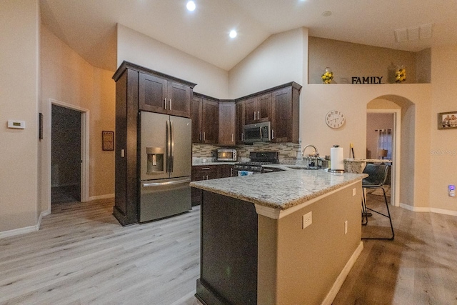 kitchen with sink, high vaulted ceiling, appliances with stainless steel finishes, a kitchen breakfast bar, and dark brown cabinetry