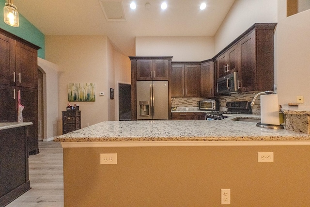 kitchen with dark brown cabinets, backsplash, kitchen peninsula, and appliances with stainless steel finishes