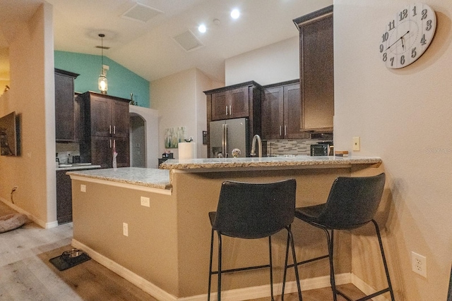 kitchen featuring a kitchen breakfast bar, kitchen peninsula, decorative backsplash, and stainless steel refrigerator with ice dispenser