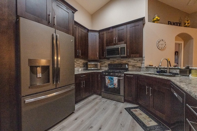 kitchen featuring stainless steel appliances, sink, vaulted ceiling, tasteful backsplash, and light stone countertops